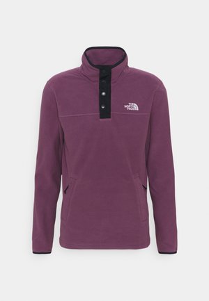 Fleece pullover in dark purple with a high collar, black placket, and button closure. Features side pockets and a logo on the chest.