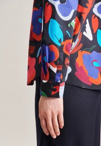 Chemise à manches longues en imprimé floral avec des fleurs multicolores sur fond noir, dotée de poignets boutonnés et d'un tissu au toucher lisse.