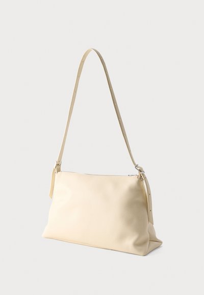 Τσάντα ώμου από δέρμα σε κρεμ χρώμα με φερμουάρ στην κορυφή και ρυθμιζόμενο λουρί, εμφανίζεται σε απλό ανοιχτό φόντο.