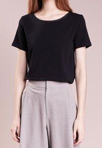 Black short-sleeve t-shirt with a round neckline, made from soft fabric, paired with light gray high-waisted trousers featuring front seams.