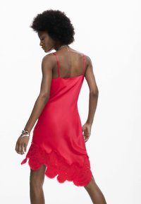 Vestido de satén rojo con tirantes finos ajustables, con un dobladillo con borde festoneado adornado con patrones florales bordados y bordes con flecos.