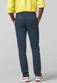 Marineblaue Chinos mit einem strukturierten gewebten mehrfarbigen Gürtel, zwei Gesäßtaschen mit Reißverschlüssen und klassischen weißen Sneakers mit roten Akzenten.