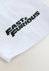 Biała tkanina z czarnym nadrukiem tekstu "FAST & FURIOUS" i widocznymi szwami w pobliżu krawędzi, na jasnej powierzchni.