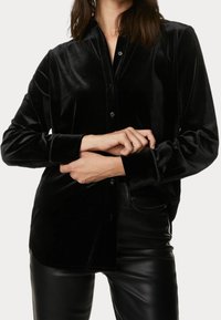 Czarna aksamitna koszula zapinana na guziki, z kołnierzykiem, długimi rękawami i gładką fakturą. Posiada prosty krój i widoczną listwę z guzikami.