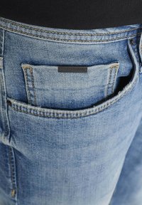 Svijetloplave traperice s lagano izblijedjelim finišom, koje imaju malu crnu oznaku na stražnjem džepu i kontrastno šivanje.