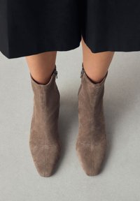 Brown suede ankle boots with a pointed toe and side zipper. The upper features stitching details and a smooth texture.