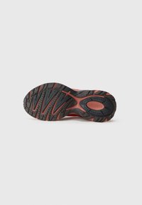 Solares de borracha preta com detalhes em vermelho, apresentando uma superfície texturizada para aderência e padrões em ziguezague únicos. Logo da Lacoste embutido na lateral.