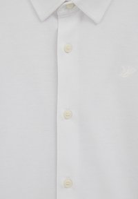Polo blanc en tissu texturé, avec un col classique et trois boutons. Comprend un logo brodé blanc subtil.