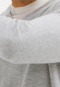 Grijze trui met een V-halsontwerp, zachte gebreide textuur en ribbelaccenten bij de halshals en manchet, deels zichtbaar in de afbeelding.