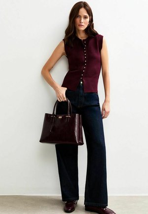 Bordeaux mouwloze top met knoopdetail, gecombineerd met donkere wijdvallende denim broek en een bijpassende bordeaux leren handtas.