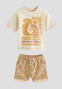 T-shirt en coton beige avec un graphisme de caméléon et de soleil en orange et rouge ; associé à un short beige avec un motif de losanges et une taille élastique.