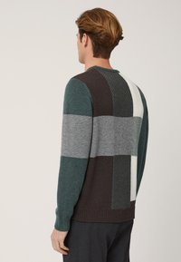 Maglione con un design a blocchi di colore nelle tonalità di teal, grigio, marrone e crema. Maglia a trama sulla parte posteriore e polsini a coste.