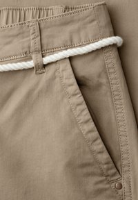 Pantalon beige avec poche latérale visible et passants de ceinture, avec une ceinture en corde blanche torsadée.