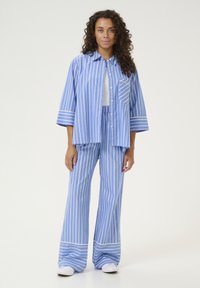 Camicia a righe blu e bianche con maniche a tre quarti e chiusura con bottoni, abbinata a pantaloni larghi a righe coordinati. Tessuto di cotone.
