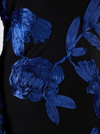 Svart tyg med upphöjd, glansig blå blommig broderi med stora kronblad och blad i texturerat bandliknande material.