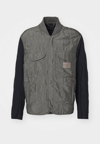 Grietas siuvinėta liemenė su juodomis rankovėmis, dviem krūtinės kišenėmis, petnešomis ir logotipo etikete kairėje pusėje. Sklandus, tekstūruotas audinys.