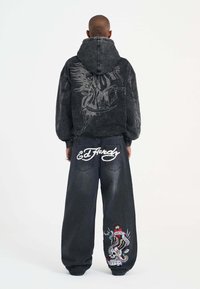 Black denim hoodie with graphic design on back, paired with loose-fitting black denim jeans featuring colorful embroidered patch and logo.