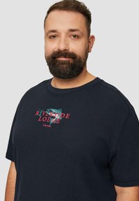 Navyblauwe T-shirt met korte mouwen en ribbeltextuur, met een meerkleurige graphic van "Riverside Lodge" en subtiele branding.