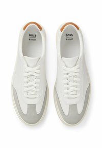 Valkoiset nahkakengät, joissa on harmaat mokkapintaiset yksityiskohdat, pyöreä kärki, nauhakiinnitys ja ruskea nahkayonkin yksityiskohta kantapäässä. Ortholite-logo näkyy sisällä.