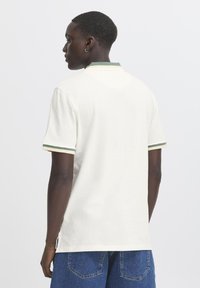 Polo blanca de algodón, con un cuello a rayas verde y beige y mangas cortas, con aberturas laterales para mayor comodidad.