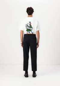 T-shirt branca com um gráfico de cartoon nas costas, combinada com calças pretas e sapatos pretos; fundo simples.