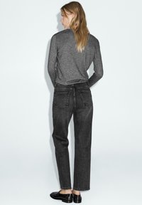 Jeans grigio scuro a vita alta con design a gamba dritta, dotati di due tasche posteriori e dettagli di cucitura sottili. Indossati con un top grigio a maniche lunghe.