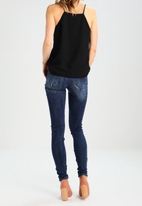 Top negro sin mangas con tirantes finos, combinado con pantalones vaqueros ajustados azul oscuro y tacones de bloque beige. Tela suave y diseño ajustado.
