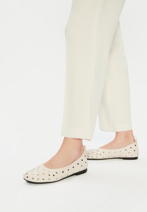 Baleriny w jasnym beżu z małymi srebrnymi ćwiekami, z okrągłym noskiem i czarną podeszwą. W zestawie z białymi, zwężanymi spodniami.