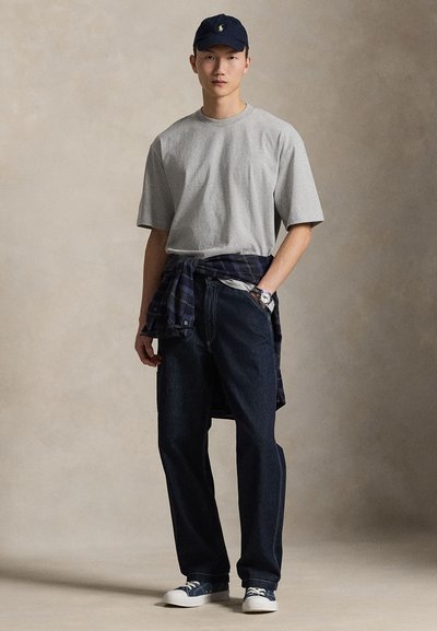 Γκρι κοντομάνικο μπλουζάκι, σκούρο μπλε τζιν, μπλε καπέλο με λογότυπο, πουκάμισο καρό δεμένο στη μέση, λευκά αθλητικά παπούτσια με μπλε λεπτομέρειες.