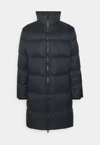 Abrigo acolchado negro con cuello alto, con cremallera frontal y diseño acolchado horizontal. Textura suave y corte hasta la rodilla.