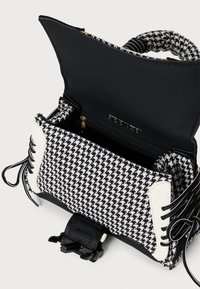 Geantă în alb și negru cu model houndstooth, cu clapeta deschisă, mânere căptușite, șireturi laterale și buzunar interior cu fermoar vizibil.