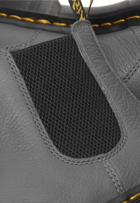 Gros plan d'une botte en cuir gris avec panneau latéral élastique noir, surpiqûres jaunes et languette avec motif noir et jaune.