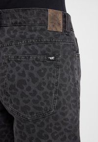 Blugi din denim cu print leopard negru, cu un patch din piele maro cu logo-ul mărcii pe spate. Au buzunare standard și detalii cusute.