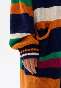 Sweter dzianinowy z wyraźnymi paskami w kolorze granatowym, pomarańczowym, zielonym i białym. Posiada dużą kieszeń oraz ściągacze w wielokolorowe akcenty.