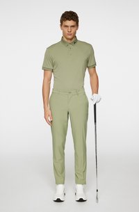 Ljusgrön golfpolo med krage och tre knappar, matchad med lätta byxor. Modellen håller en golfklubba och bär vita sneakers.