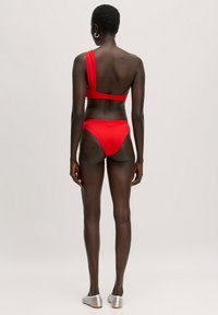 Roter Ein-Schulter-Bikini-Oberteil mit verstellbarem Rückenverschluss, kombiniert mit hüfttiefen, einfarbigen roten Bikiniunterteilen, glatte Textur, minimales Design.