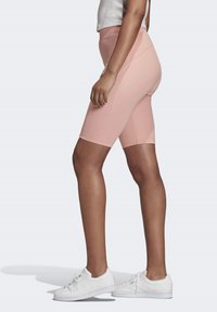 Ljust rosa cykelbyxor med hög midja och mjuk textur, kombinerat med vita sneakers, visat från sidovyn.