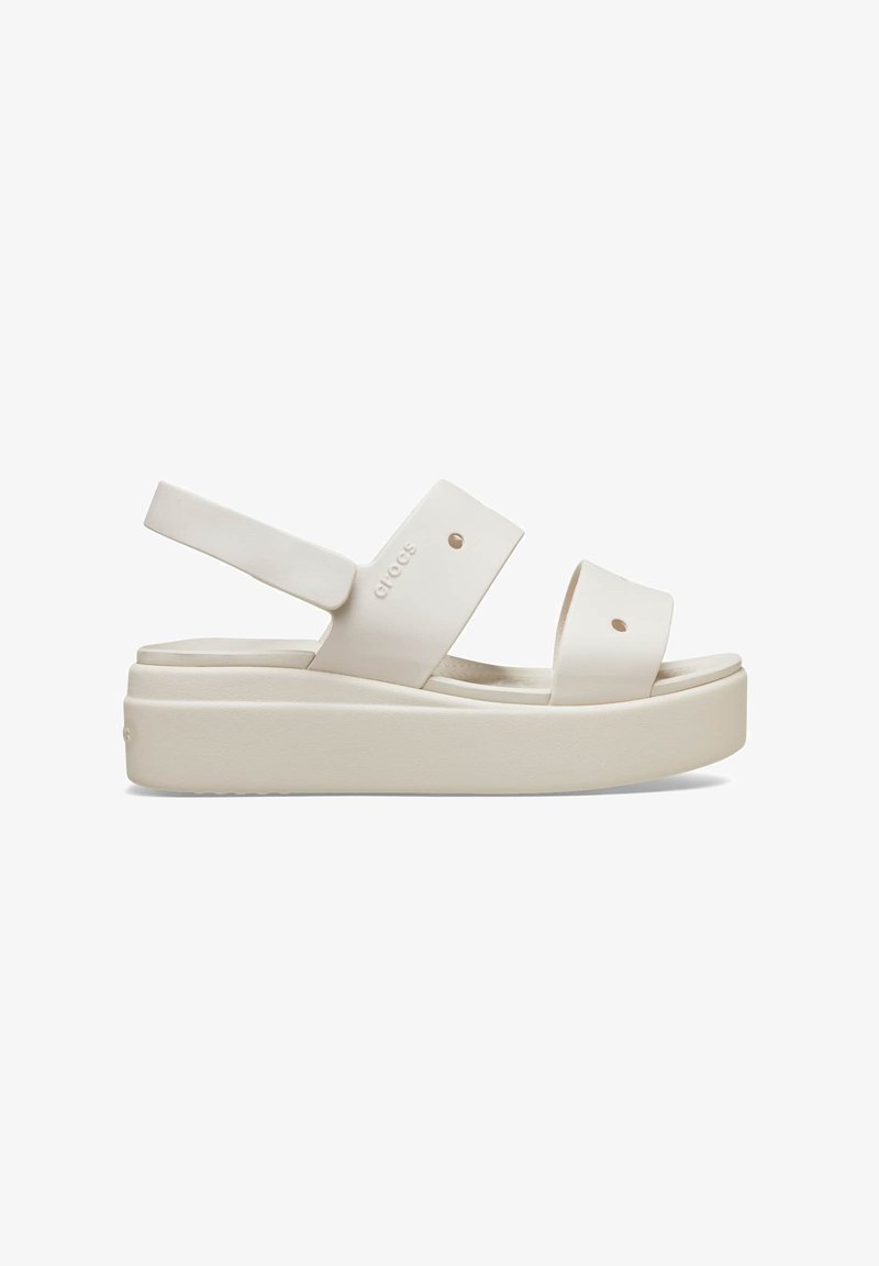 White platform sandals with wide straps, made of smooth material, featuring adjustable back strap and pronounced sole. Minimalistic design.