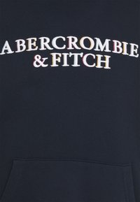 Felpa blu navy con grande logo ricamato "ABERCROMBIE & FITCH" in bianco, giallo e rosso. Include una tasca a canguro sul davanti.