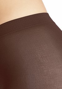Leggings marroni con una superficie liscia e strutturata e una cintura ampia, esposti su uno sfondo di pelle chiara.