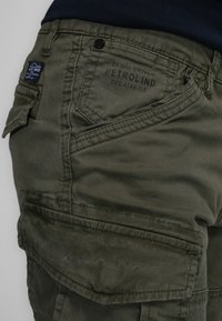 Groene cargobroek met een zachte textuur, meerdere zakken en gestikte details. Heeft een merklabel op de achterzak.