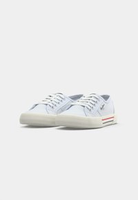 Lavtop hvide lærredssneakers med hvide snørebånd, tykke teksturerede gummisåler, rød og blå stribe på siden og mærkelogo på hælen.