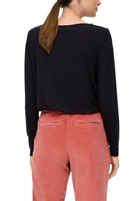 Zwarte langemouwen top met een losse pasvorm, gecombineerd met roze corduroybroeken met verticale ribbels en achterzakken.