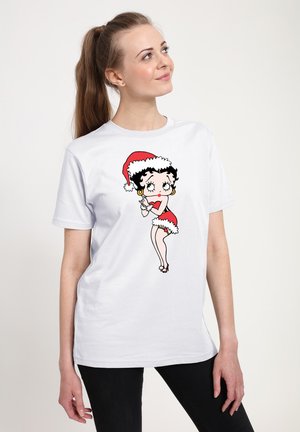 Hvid t-shirt med en tegneseriefigur i en rød julesweater med hvidt trim. Korte ærmer, afslappet pasform og sorte bukser nederst.