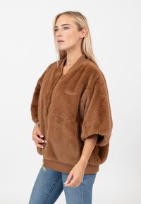 Brązowa kurtka z sztucznego futra z zamkiem z przodu, szerokimi krótkimi rękawami i prążkowanymi mankietami. Miękka tekstura i prosty design bez dodatkowych wzorów.