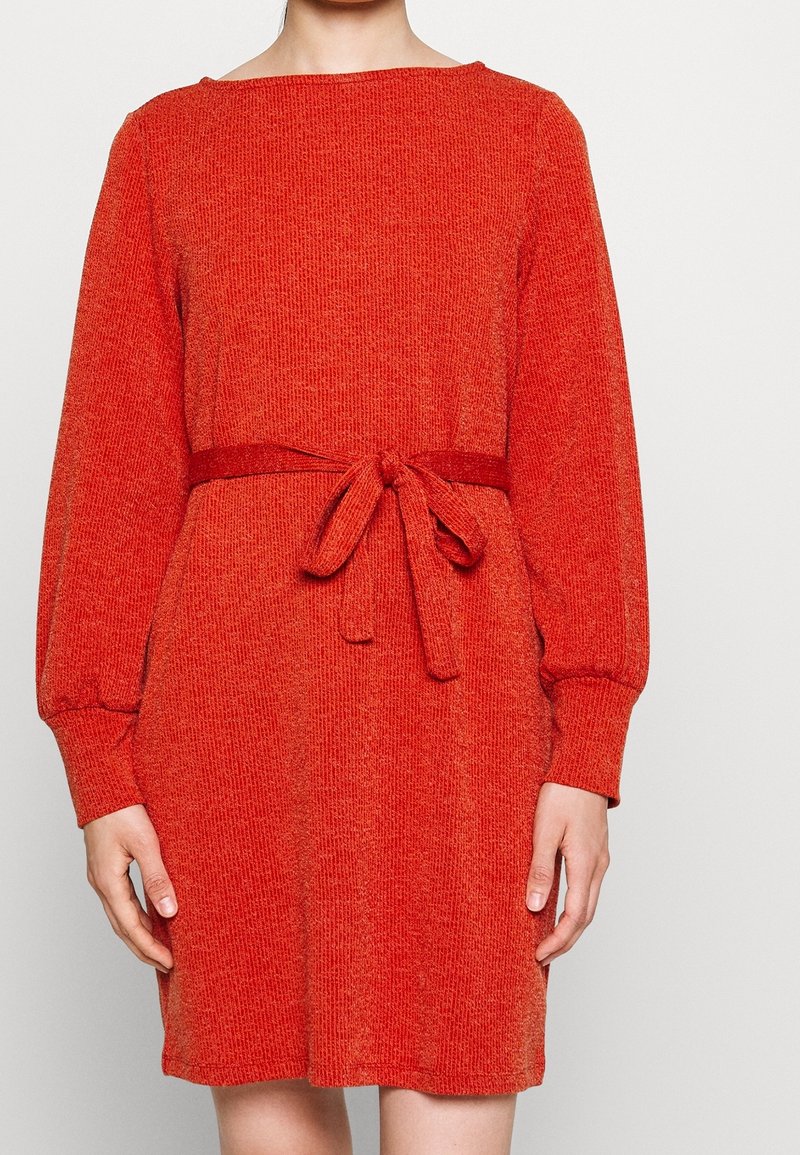 Vestido de punto rojo con mangas largas abullonadas y un cinturón de tela atado en la cintura. La textura es suave y ligeramente acanalada en toda su superficie.