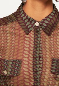 Camicia trasparente a fantasia nei toni del bordeaux, verde e giallo. Presenta un colletto, chiusure con bottoni e due tasche frontali con dettagli a patta.