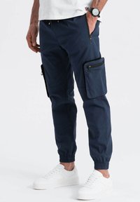 Pantalons cargo de marine avec des poignets élastiques, des poches zippées sur les côtés et des accents noirs contrastants, fabriqués en tissu lisse.