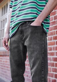 Grå jeans med en smal passform, med en klassisk femficksdesign och synlig sömnad. Kombinationen med en grön och randig skjorta.