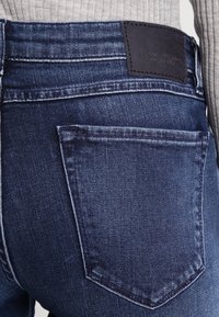 Mörkblå denimjeans med en strukturerad passform; har en bakficka och en svart läderlapp i midjan med präglad text.